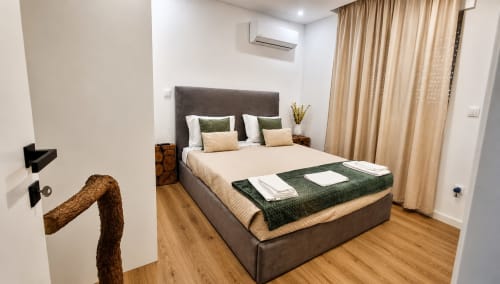 Quarto moderno da casa Serração em Gerês com cama estofada cinzenta, roupa de cama bege, acentos verdes e piso em madeira