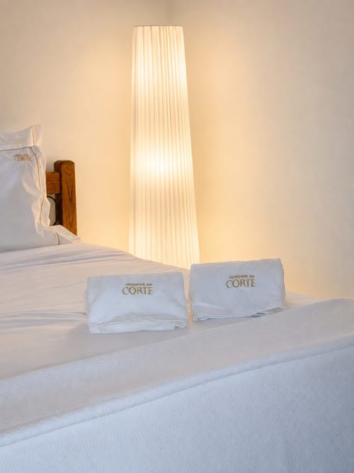 Cama de luxo com roupa de cama branca e almofadas personalizadas no hotel rural Herdade da Corte em Tavira, Portugal, com iluminação alta