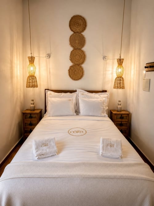 Quarto elegante na Herdade da Côrte com cama em branco, decoração de parede trançada, criados em madeira e iluminação pendente