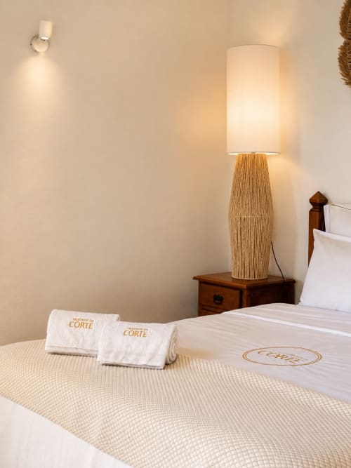 Quarto na Herdade da Côrte com luminária tecida, toalhas enroladas e cama branca com vista para a piscina