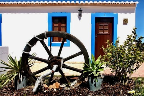Rustic cottage exterior at Herdade da Côrte with white walls, blue accents, wooden doors, and decorative wagon wheel in