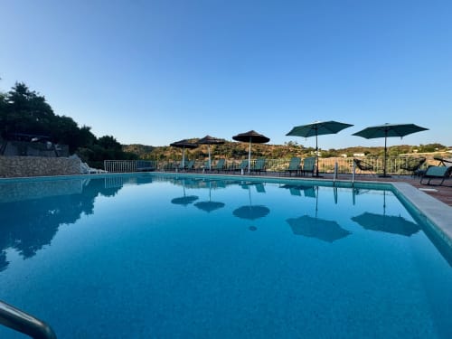 Piscina azul cristalina com guarda-sóis e espreguiçadeiras com vista para a zona rural na Herdade da Côrte, Portugal