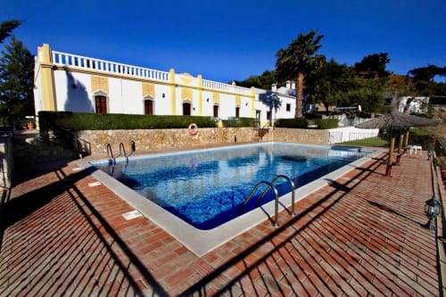 Piscina retangular azul com escada na Herdade da Côrte, hotel rural em Tavira, Portugal, edifício branco com detalhes amarelos
