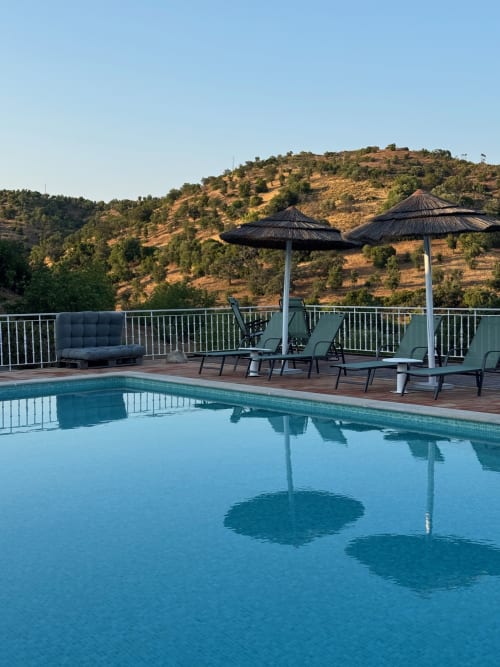 Terraço luxuoso com piscina no Turismo Rural Herdade da Côrte em Tavira, Portugal, com espreguiçadeiras, guarda-sóis e vistas da serra