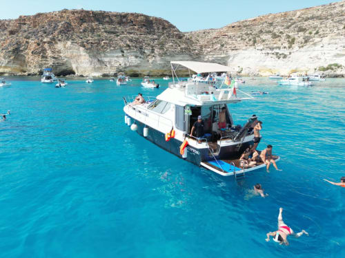 Acque turchesi di Lampedusa con turisti che nuotano e navigano presso scogliere rocciose