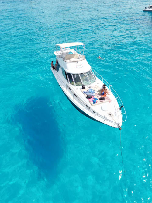 Lussuoso yacht bianco ancorato nelle acque turchesi di Lampedusa, Italia con ospiti che si rilassano sul ponte