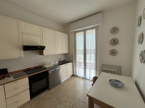 Cucina luminosa nell'appartamento B&B di Verona con mobili color crema, elettrodomestici neri, tavolo da pranzo e accesso al balcone