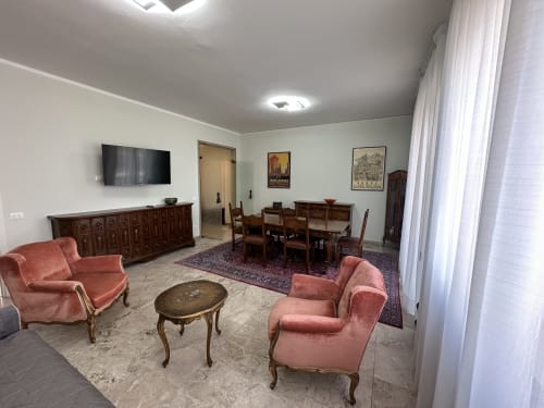 Elegante soggiorno con sedie in velluto rosa, tavolo da pranzo in legno e TV a schermo piatto presso 10 Minutes B&B Verona