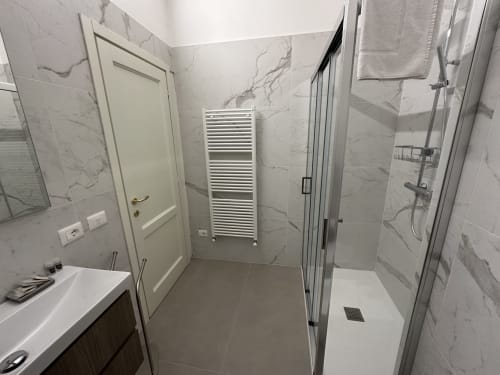 Bagno moderno al 10 Minutes B&B di Verona con piastrelle in marmo, doccia walk-in, scaldasalviette e vanity bianca.