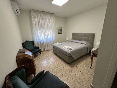 Spaciosa camera da letto al 10 Minutes B&B Verona con letto imbottito grigio, zona living, ampie finestre e pavimento in terrazzo.