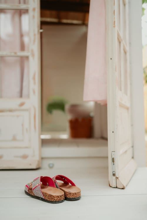 Sandales de liège rouge sur sol blanc, portes ouvertes sur chambre rose à la Bleu Guest House, Saint-François
