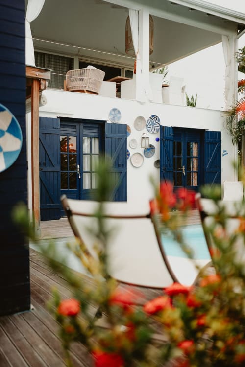 Patio de la Bleu Guest House avec portes bleu marine, murs blancs, assiettes décoratives et fleurs rouges à Saint-François