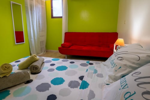 Chambre lumineuse aux Gîtes Bagatelle avec murs vert citron, canapé rouge, lit à motifs et serviettes roulées