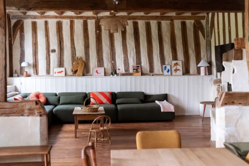 Villa moderne Maisons Noisette : salon avec canapé sectionnel vert, poutres bois et vue sur le jardin