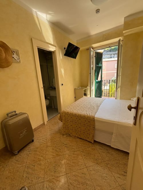 Chambre simple avec balcon à l'Hôtel Feluca à Bonassola, murs jaunes, lit, TV et vue sur le jardin
