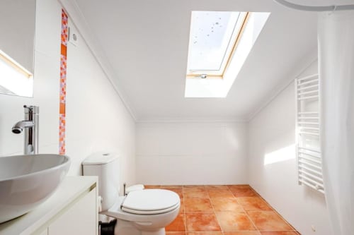 Modern bathroom in Chaves villa with skylight, white fixtures, orange tile flooring, and heated towel rack