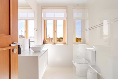 Modern luxury bathroom in Chaves villa with white fixtures, wooden-framed windows, garden views, and contemporary design