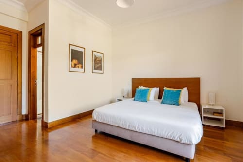 Spacious bedroom in Chaves villa with queen bed, wooden headboard, turquoise pillows, hardwood floors, and garden view