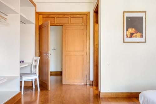 Modern villa bedroom in Chaves with wooden doors, desk, chair, and garden view artwork on cream walls
