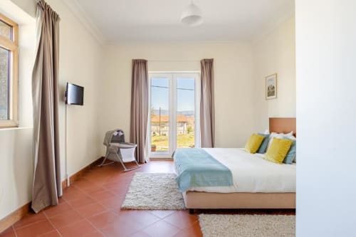 Spacious bedroom in Chaves villa with terracotta tile floor, garden view doors, TV, tan curtains, and tan upholstered bed