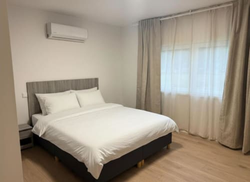 Modern bedroom with white bedding, gray headboard, air conditioning unit, and garden view curtains in Chaves villa