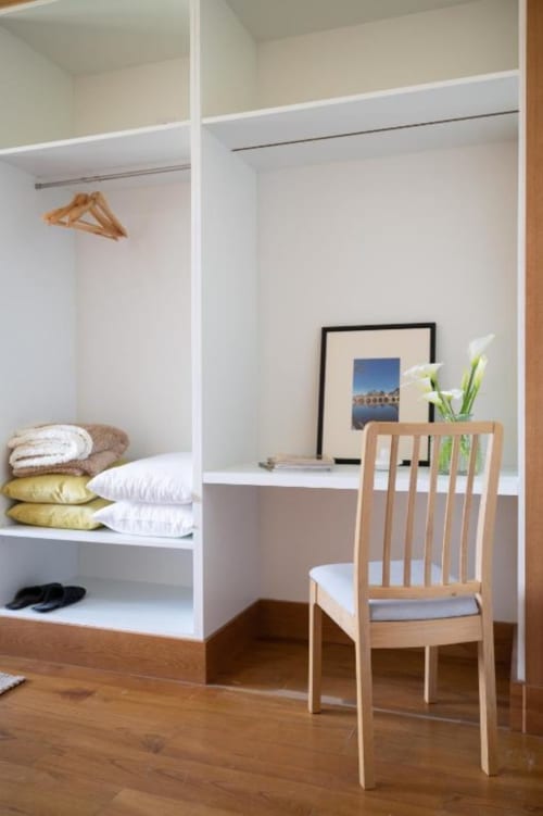 Modern bedroom in Chaves villa with built-in white shelving, wooden chair, desk with framed art, and organized bedding