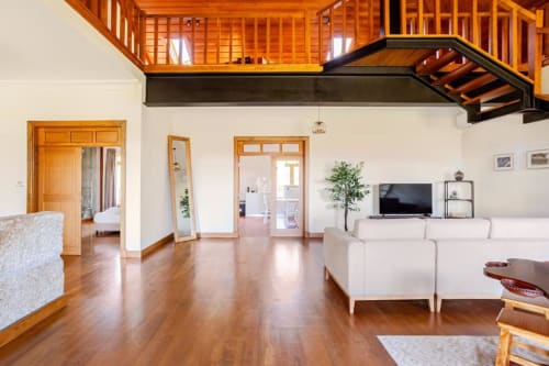 Spacious villa living room in Chaves with wooden mezzanine, white sofa, hardwood floors, and garden views