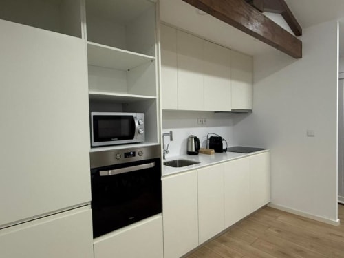 Modern kitchen in Chaves villa with white cabinetry, stainless steel appliances, microwave, and wooden beam ceiling