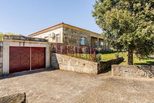 Stone villa in Chaves with red garage doors, terrace, garden views, and lush green surroundings