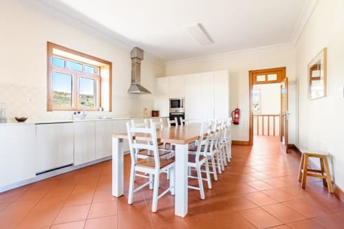 Modern kitchen and dining area in Chaves villa with white cabinetry, wooden table, terracotta floors, and garden views