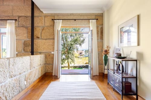 Stone villa hallway with wooden floors, cream curtains, and garden view in Chaves, Portugal