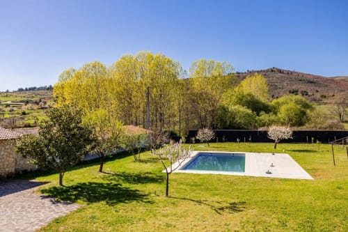 Spacious villa garden in Chaves with swimming pool, lush green lawn, blooming trees, and mountain views