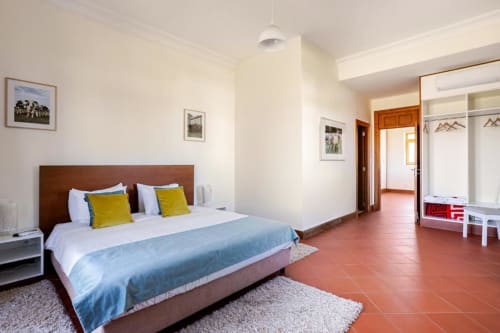 Spacious bedroom with wooden bed, yellow pillows, terracotta floor, and wardrobe access in Chaves villa