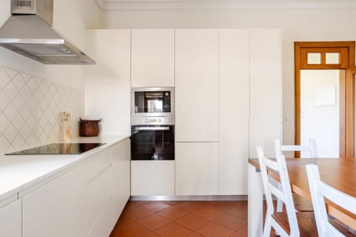 Modern white kitchen with built-in oven, dining area, and wooden door in Chaves villa rental