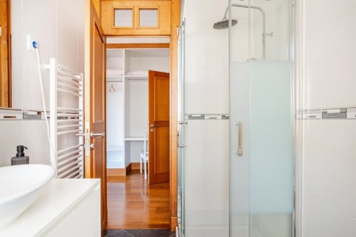 Modern bathroom in Chaves villa with shower, sink, heated towel rack, and open wooden door to bedroom