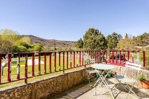 Sunny terrace with red railing, dining table, and garden views at Chaves villa in Portugal