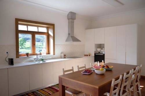 Modern white kitchen with wooden dining table, stainless steel range hood, and garden views in Portuguese villa