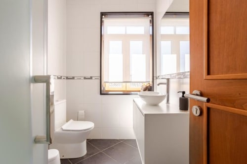 Modern bathroom in Chaves villa with white vanity, vessel sink, toilet, and garden views through framed window