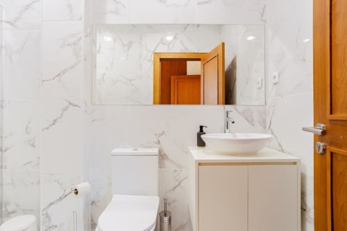 Modern bathroom in Chaves villa with marble walls, vessel sink, wooden vanity, mirror, and white toilet