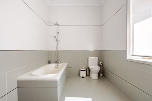 Modern bathroom in Chaves villa with bathtub, shower, toilet, beige tile walls, and window with garden view