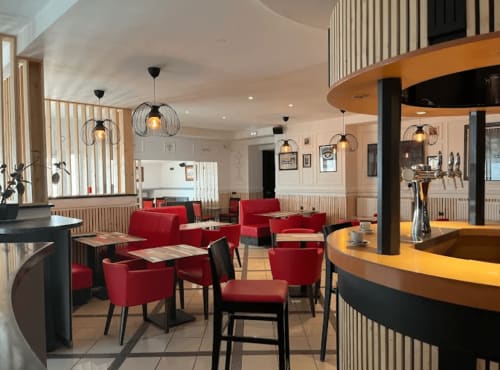 Hall d'accueil moderne à l'Hôtel Norotel Brumath avec sièges rouges, luminaires suspendus et comptoir bar en bois