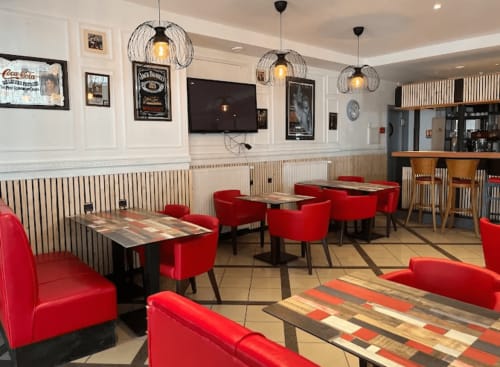 Hôtel Norotel Brumath reception hall with red modern chairs, wooden tables, pendant lights, and wainscoting paneling.