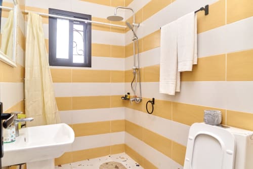 Salle de bains moderne de l'Hôtel Yakro à Yamoussoukro avec carrelage jaune et blanc rayé, douche, toilettes et lavabo