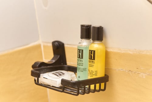 Étagère noire de salle de bains à l'Hôtel Yakro avec articles de toilette : savon, gel douche vert et flacon de shampooing jaune