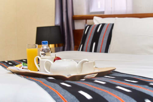 Petit-déjeuner en chambre standard de l'Hôtel Yakro : jus, théière et chemin de table rayé sur table blanche
