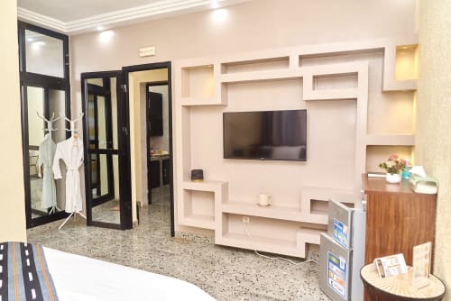 Chambre standard de l'Hôtel Yakro à Yamoussoukro avec téléviseur, étagères murales, mobilier moderne et salle de bains privative