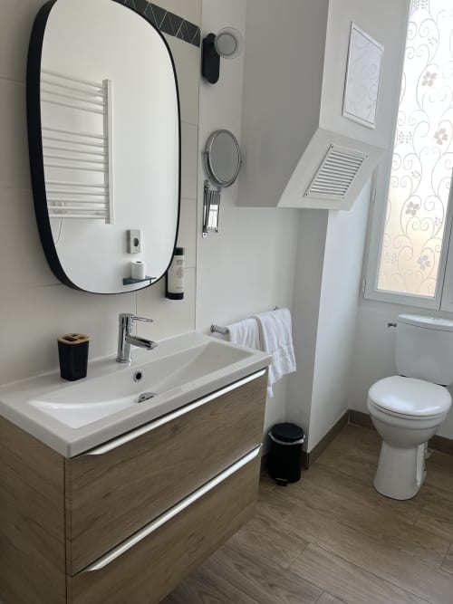 Salle de bains moderne de l'Hôtel Les Paquebots avec vanité, miroir à cadre noir, toilettes et revêtement de sol aspect bois