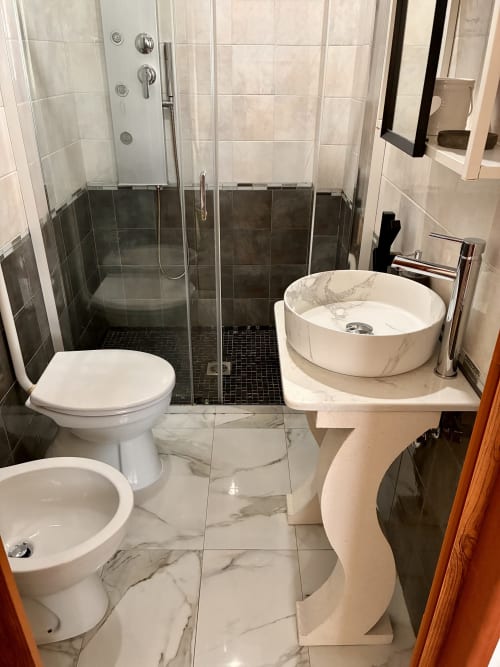 Modern bathroom at Noemi Holiday House with marble details, round vessel sink, glass-enclosed shower, wc and bidet.