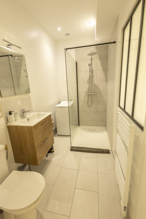 Salle de bains moderne du gîte Accolade avec douche à l'italienne, meuble vasque en bois et carrelage blanc à Châteaudun