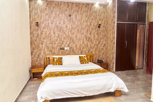 Suite moderne de l'Hôtel Yakro à Yamoussoukro avec lit queen, carrelage en mosaïque, meubles en bois et TV écran plat